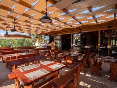 Überdachter Außenbereich eines Restaurants mit Holztischen und Stühlen, Lichtspiel durch Dachfenster.