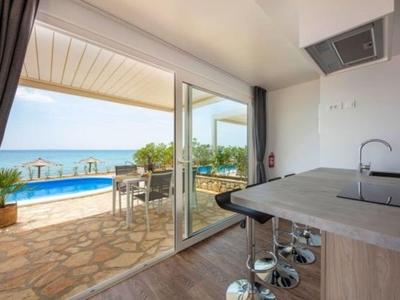 Moderner Hotelraum mit Küchenzeile und Zugang zu Terrasse mit Pool und Meerblick.