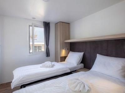 Ein helles Hotelzimmer mit zwei Einzelbetten, weißer Bettwäsche und einem Fenster mit Vorhang.