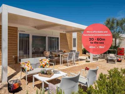 Haus mit überdachter Terrasse, Esstisch und Gartenstühlen in sonnigem Urlaubsgebiet.