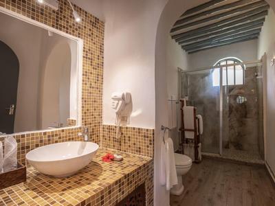 Badezimmer mit Dusche, weißem Waschbecken auf braunem Mosaik-Waschtisch und großem Spiegel.