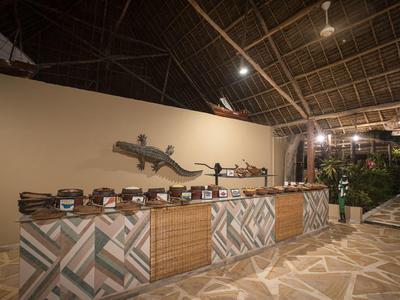 Freiluft-Buffet mit Holztheke, geometrischen Fliesen und großem Gecko an der Wand.