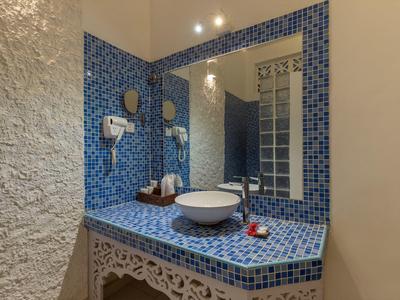 Badezimmer mit blau gekacheltem Waschbecken, rundem Spiegel und Haartrockner an weißer Wand.