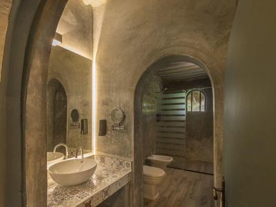 Rustikales Badezimmer mit Marmorwaschbecken, runden Spiegeln und natürlichen Steinwänden.