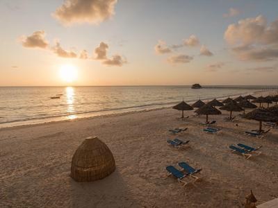 Strand mit Sand, blauen Liegestühlen und Sonnenschirmen bei Sonnenuntergang am ruhigen Meer.