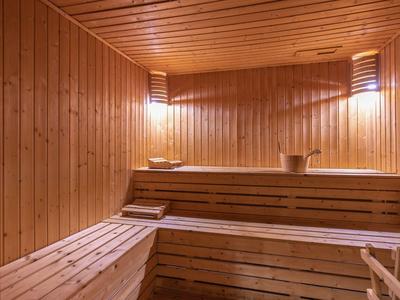 Innenraum einer Sauna mit Holzbänken, Holzwänden und sanfter Beleuchtung an der Decke.
