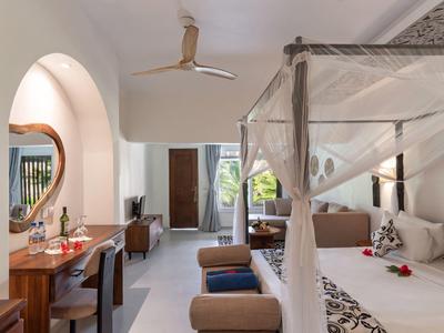 Helles Hotelzimmer mit Himmelbett, Schreibtisch, Spiegel und Blick auf eine Terrasse.