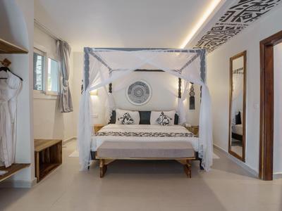 Modernes, helles Hotelzimmer mit Himmelbett, Sitzbank und offener Garderobe.