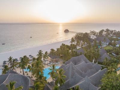 Strandresort mit Palmen, Pool und strohgedeckten Hütten am ruhigen Meer bei Sonnenuntergang.