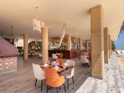 Offenes, modernes Restaurant mit Terrassenblick, Holzsäulen, gemischten Stühlen und elegant gedeckten Tischen.
