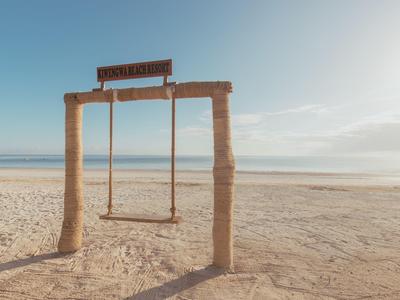 Schaukel aus Holz auf einem breiten, sandigen Strand mit ruhigem, blauem Himmel im Hintergrund.