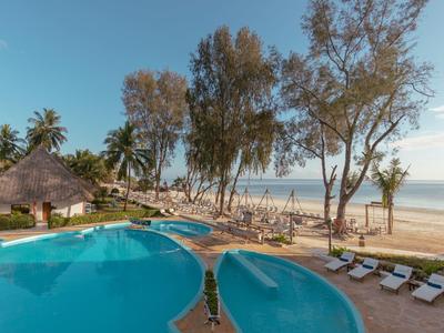 Ein blauer Pool mit Liegestühlen, Palmen und Strand unter klarem Himmel.