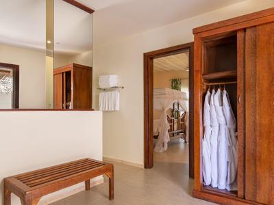 Ein heller Raum mit Holzmöbeln, weißem Wandregal, Spiegel und einer offenen Garderobe mit weißen Bademänteln.