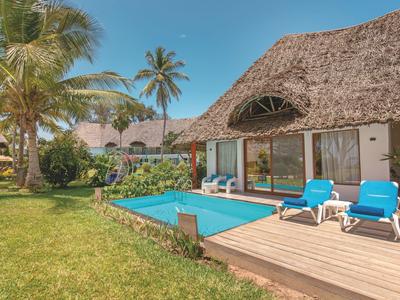 Ferienbungalows mit Strohdach, Pool und blauen Liegestühlen, umgeben von Palmen und Rasen.