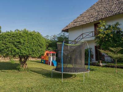 Ein Garten mit grünem Rasen, Baum, Trampolin und Kinderspielhaus neben einem hellen Haus.