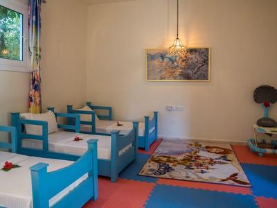 Ein helles Klassenzimmer mit blauen Holztischen, buntem Teppich und bunter Vorhangdeko.
