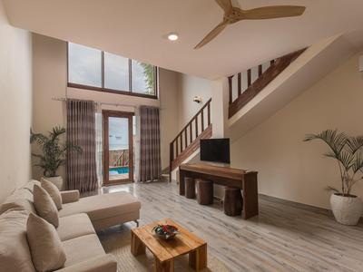 Wohnzimmer mit beiger Couch, Holztisch, TV und Treppe zu einer oberen Etage mit Blick auf den Pool.