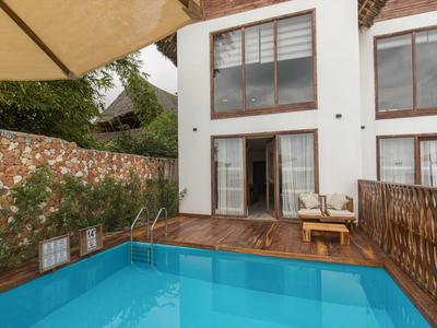 Moderner Pool vor einem Haus mit Terrasse, Stühlen und Sonnenschirm.