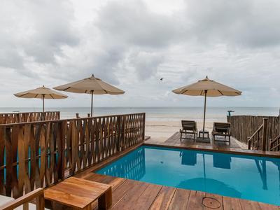 Moderner Poolbereich mit Holzdeck, Sonnenschirmen und Blick auf das Meer unter bewölktem Himmel.