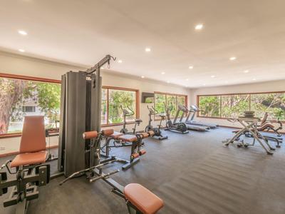 Großer, heller Fitnessraum mit mehreren Trainingsgeräten und großen Fenstern, die viel Tageslicht spenden.