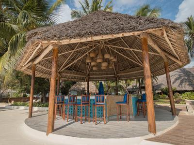 Offener Strand-Barbereich mit Strohdach, Holzsäulen und blauen Barhockern in tropischer Umgebung.