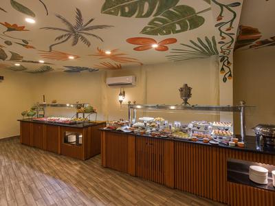 Buffetraum mit Holztheken, verschiedenem Essen und Decke mit großen Pflanzenmotiven in warmem Licht.