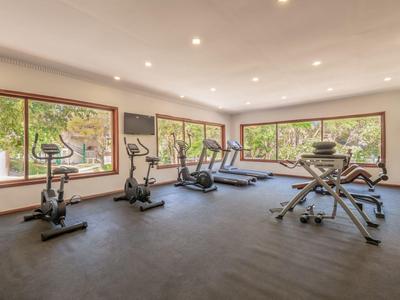 Helles Fitnessstudio mit großen Fenstern, mehreren Trainingsgeräten und dunkelgrauem Boden.