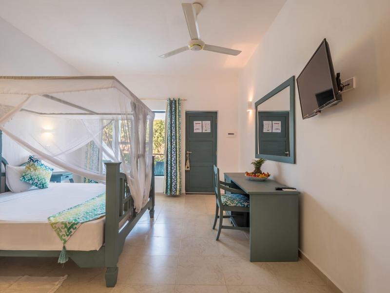 Helles Hotelzimmer mit Himmelbett, Schreibtisch, Stuhl und Wandfernseher.