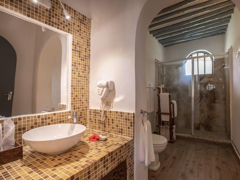 Modernes Badezimmer mit Mosaikfliesen, Rundwaschbecken, großem Spiegel und Duschbereich im Hintergrund.