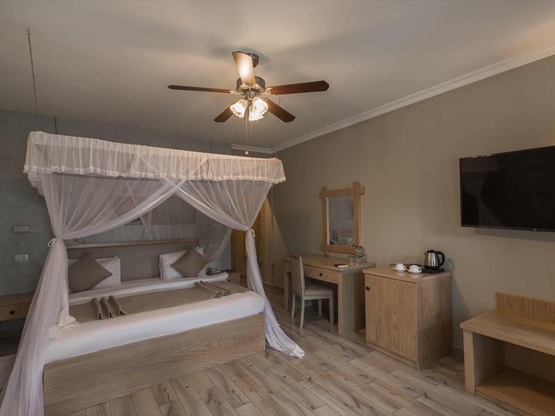 Ein Hotelzimmer mit Himmelbett, Deckenventilator, Spiegel, Fernseher und Holzmöbeln.