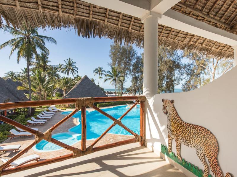 Blick von einer Terrasse mit Holzgeländer auf einen Pool und tropische Pflanzen.