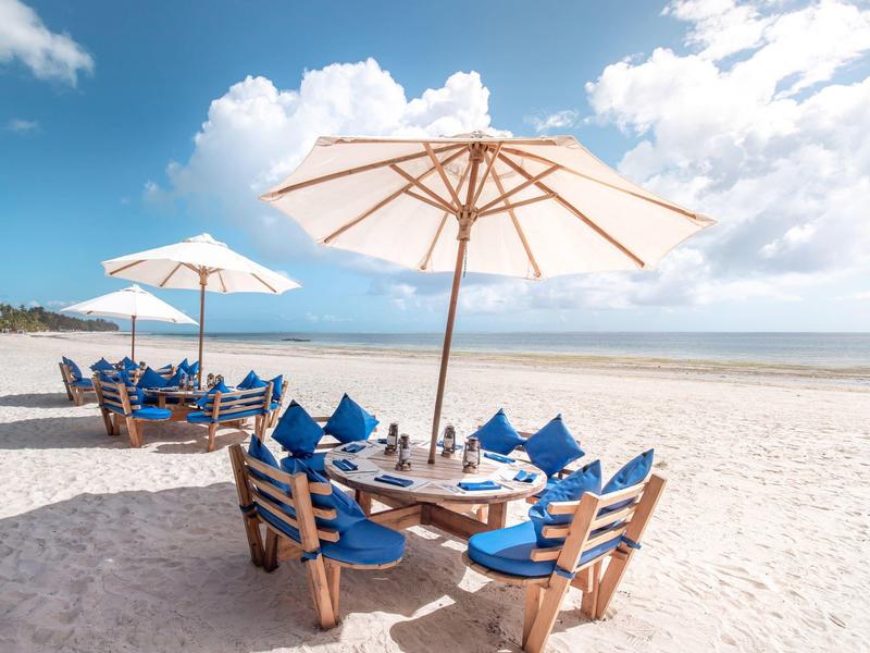 Strand mit Sand, Holztischen, blauen Kissen und Sonnenschirmen unter blauem Himmel