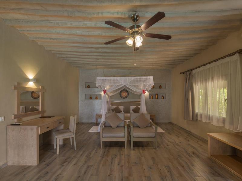 Gemütliches Hotelzimmer mit Doppelbett, Schreibtisch, Deckenventilator und Fenster mit Vorhängen.