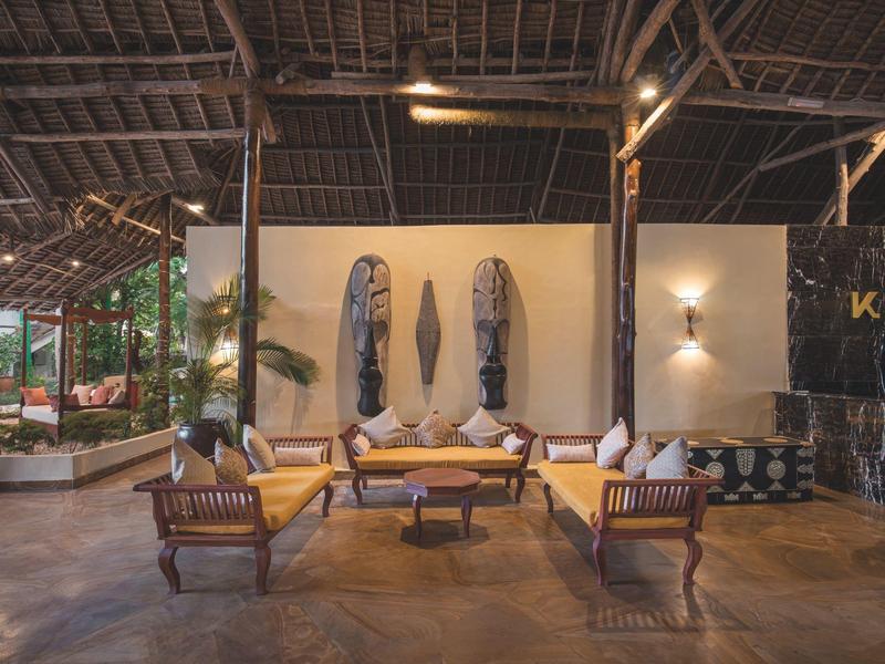 Gemütlicher Sitzbereich in offener Lobby mit Holzmöbeln und dekorativen Masken an der Wand.