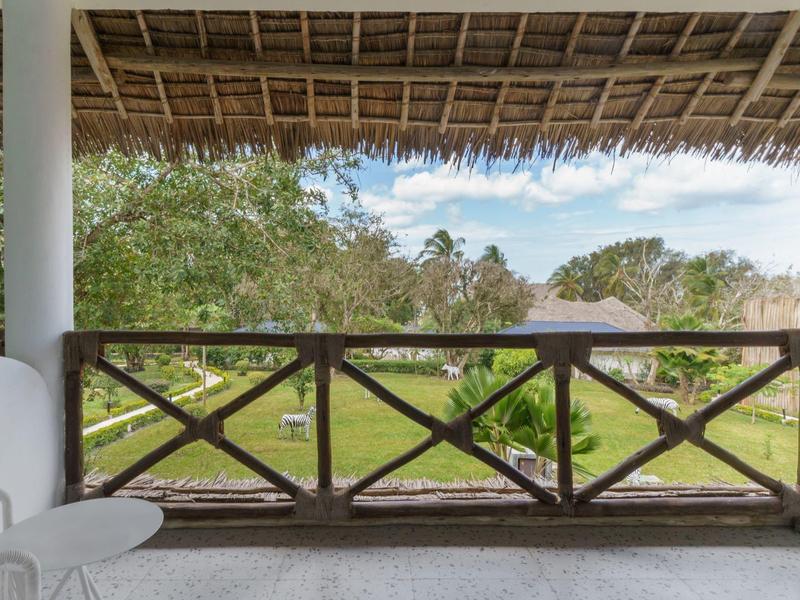Blick von einer überdachten Terrasse auf einen Garten mit Rasen und Bäumen hinter einem Holzzaun.