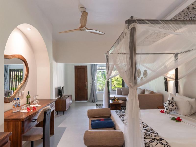 Helles Hotelzimmer mit Himmelbett, Schreibtisch, Spiegel und Blick auf eine Terrasse.