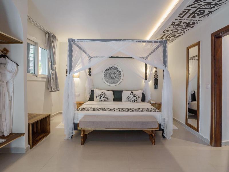 Modernes, helles Hotelzimmer mit Himmelbett, Sitzbank und offener Garderobe.