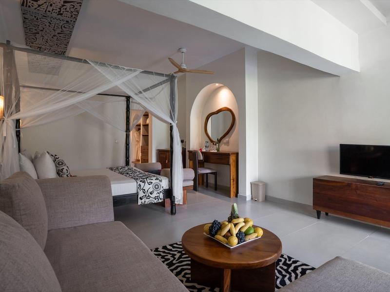 Moderner Hotelraum mit offenem Bett, Sofa, TV und rustikalem Holzmöbel.