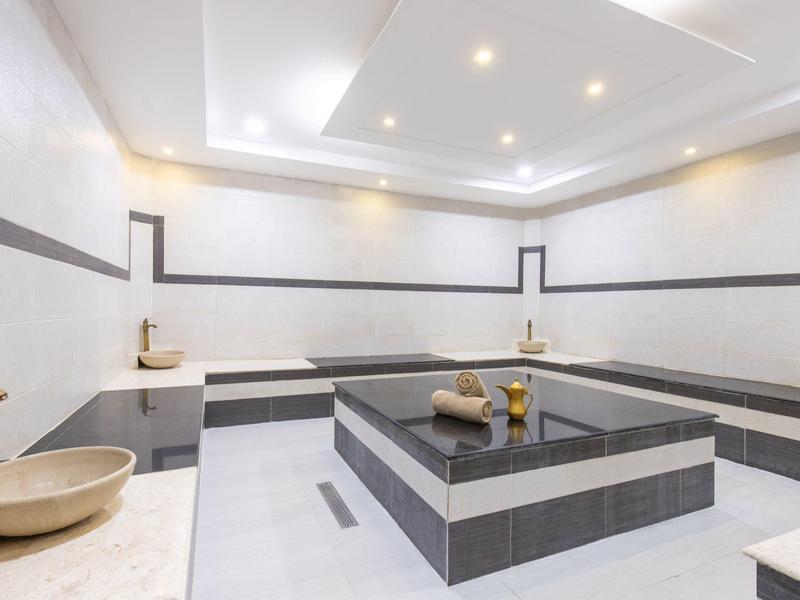 Moderner Wellnessbereich mit großem, quadratischem Whirlpool und Sitzbereichen aus Fliesen.