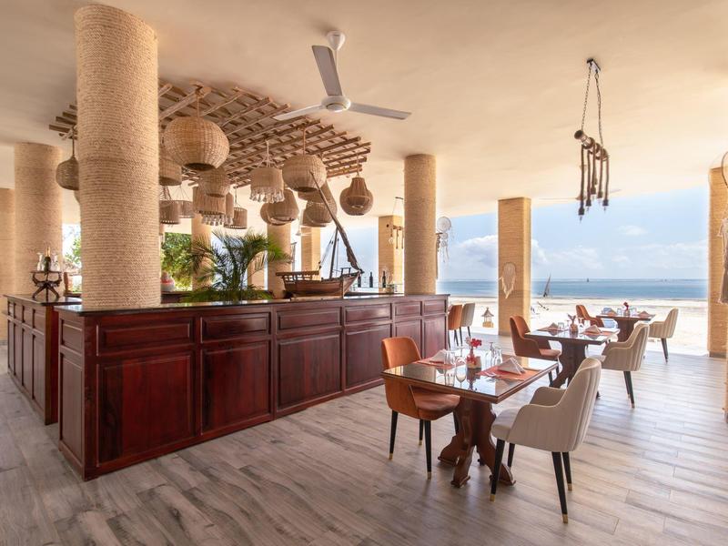 Helles, offenes Restaurant mit Holzmöbeln, Ventilatoren und Meerblick durch große Fenster.