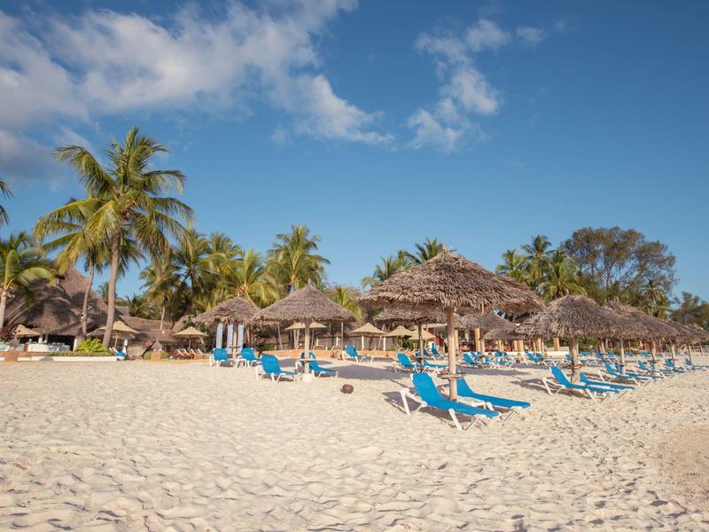 Strand mit Palmen, Sonnenschirmen und blauen Liegestühlen unter klarem Himmel.