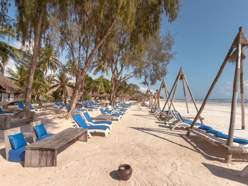 Strand mit blauen Liegen, Hängematten und Palmen unter klarem Himmel am Hotel