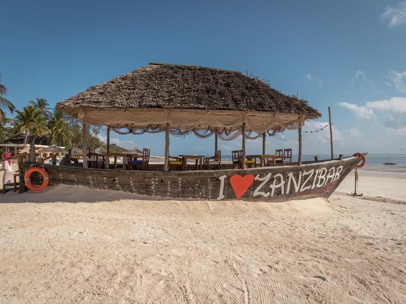Strandbar aus Holz mit Strohdach am Sandstrand unter blauem Himmel