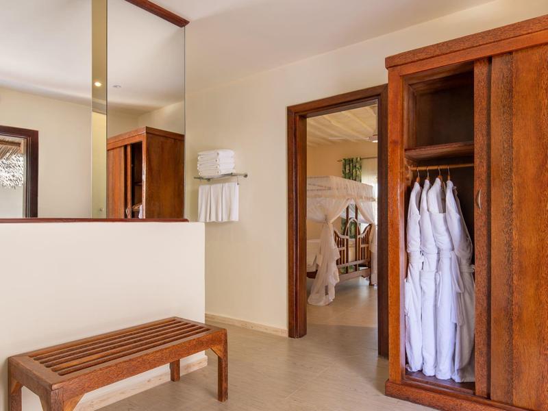 Helles Hotelzimmer mit Holzbänken, offenem Kleiderschrank und weißen Bademänteln.