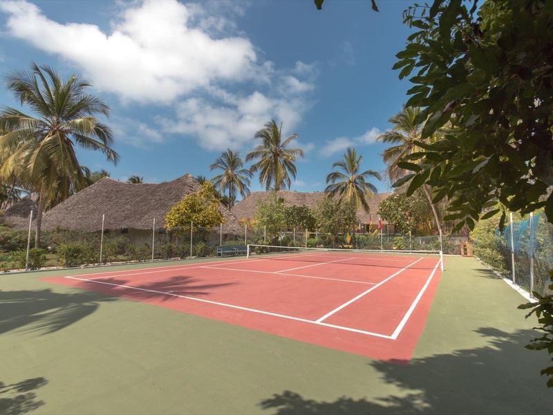 Outdoor-Tenniscourt mit Palmen und Strohdachhütten im Hintergrund unter blauem Himmel.