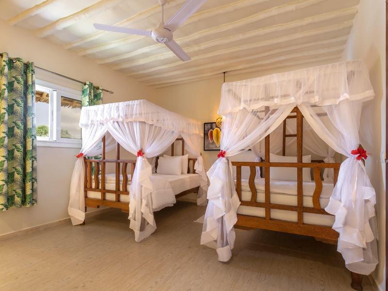 Freiluft-Tennisplatz mit rotem Belag, umgeben von Palmen und grüner Vegetation unter blauem Himmel