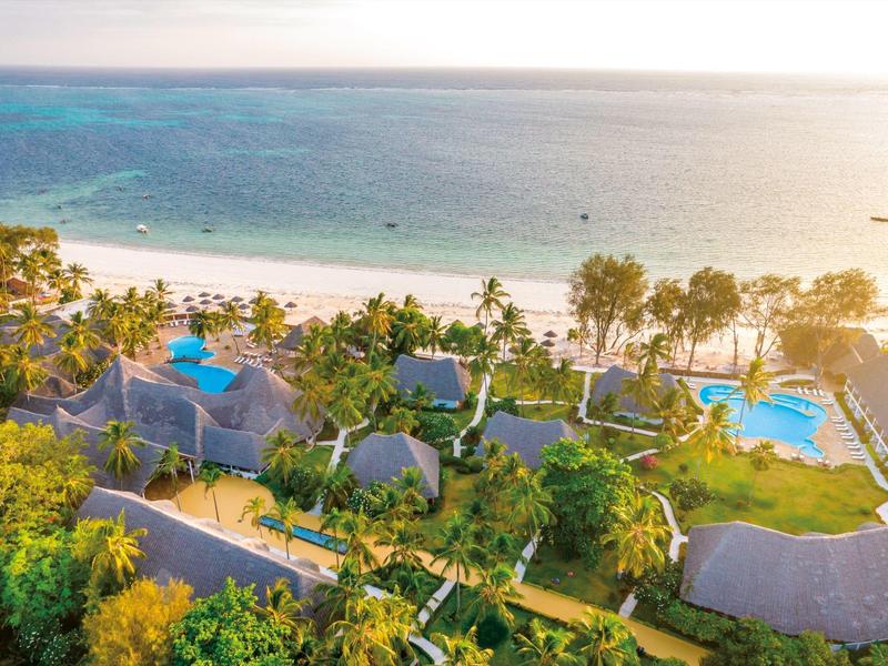 Luftaufnahme eines Resorts am Strand mit Pool, Palmen und Meerblick bei Sonnenschein.