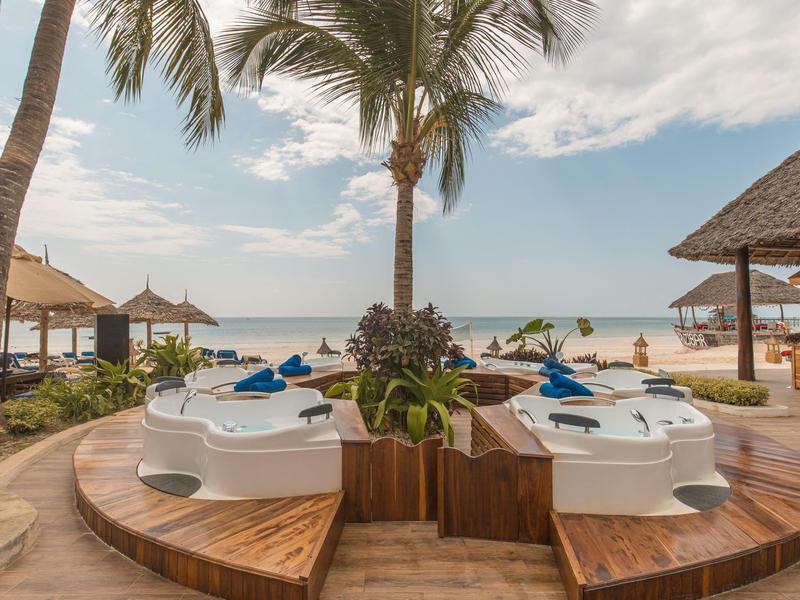Luxuriöse Whirlpools mit Blick auf den Strand und Palmen bei bewölktem Himmel.