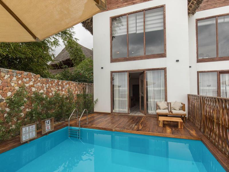 Moderner Pool vor einem Haus mit Terrasse, Stühlen und Sonnenschirm.