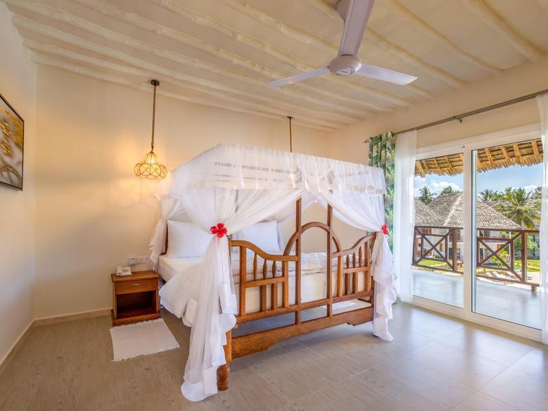 Hell eingerichtetes Schlafzimmer mit Himmelbett, Moskitonetz und Balkon mit Blick ins Grüne.